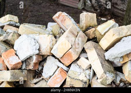 Ein Haufen alter gebrauchter Ziegelsteine mit Kratzern und Rissen von der alten Mauer in der Nähe des Grundstücks. Stockfoto