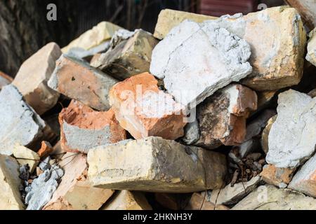 Ein Haufen alter gebrauchter Ziegelsteine mit Kratzern und Rissen von der alten Mauer in der Nähe des Grundstücks. Stockfoto