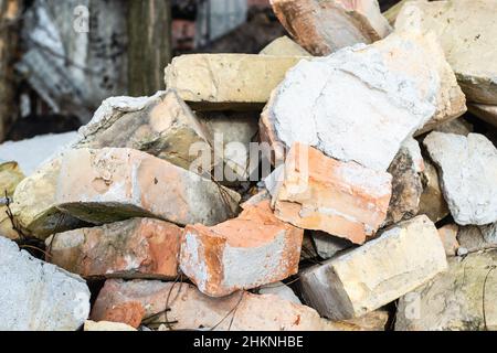 Ein Haufen alter gebrauchter Ziegelsteine mit Kratzern und Rissen von der alten Mauer in der Nähe des Grundstücks. Stockfoto