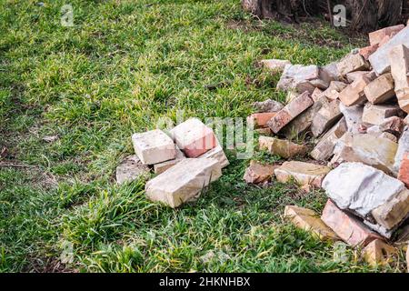 Ein Haufen alter gebrauchter Ziegelsteine mit Kratzern und Rissen von der alten Mauer in der Nähe des Grundstücks. Stockfoto