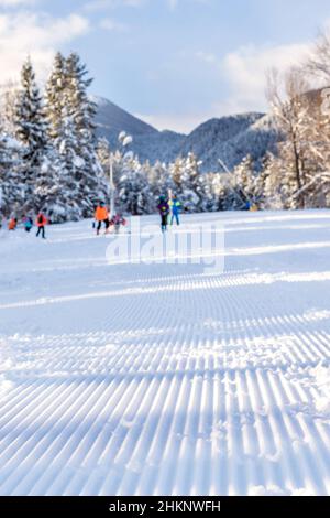 Bansko, Bulgarien Aussicht auf frisch präparierte Skipiste und defokussierte Berggipfel und Skifahrer Stockfoto