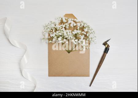 Kalligrafische Feder und Frühlingsumschlag mit Blumen und weißem Band, Grußkarte für Valentinstag mit Platz für Ihren Text. Flach liegend, Draufsicht Stockfoto