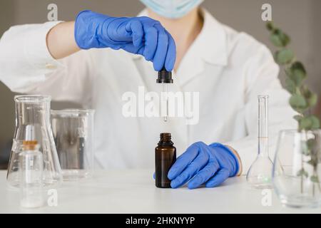 Apothekerin beim Öffnen der Pipettentropfer mit einem Tropfen natürlichen Öls über der Glasflasche. Labortests von Kosmetika. Stockfoto