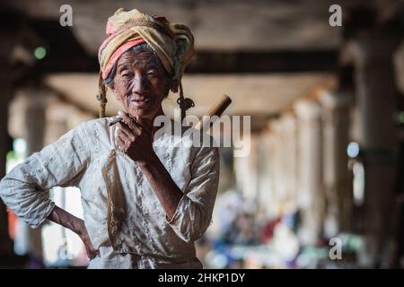 Eine alte burmesische Dame raucht eine Zigarre auf dem traditionellen Handwerksmarkt im Dorf Indein, Shan State, Myanmar (Burma). Stockfoto