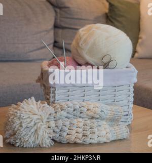 Rosa und weiße Wollkugeln in einem weißen Korb mit Stricknadeln und einem handgefertigten Strickhut Stockfoto