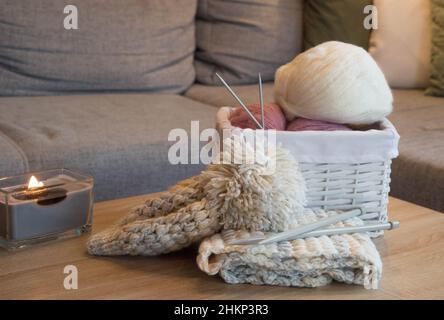 Rosa und weiße Wollkugeln in einem weißen Korb mit Stricknadeln und einem gestrickten Schal und Hut handgefertigt Stockfoto