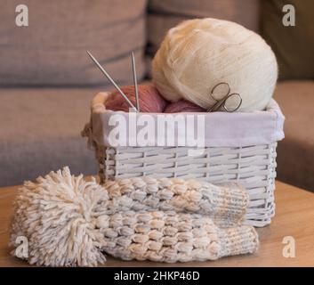 Rosa und weiße Wollkugeln in einem weißen Korb mit Stricknadeln und einem handgefertigten Strickhut Stockfoto