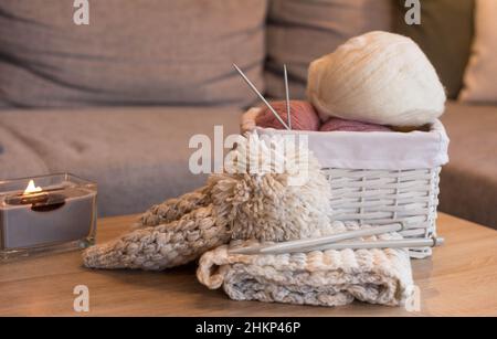 Rosa und weiße Wollkugeln in einem weißen Korb mit Stricknadeln und einem handgefertigten Strickhut Stockfoto