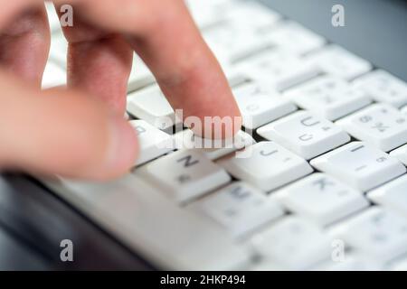 Fingerdruck auf eine einzelne Taste auf einer weißen Laptop-Tastatur, flacher freiheitsgrad, Objektmakro, Detail, extreme Nahaufnahme. Verwendung eines Computers, Benutzererfahrung, inte Stockfoto