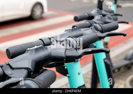 Einfache Elektroroller auf der Straße geparkt, Bürgersteig, Detail, Griff Bars in der Nähe, niemand, zebrastreifen, Auto im Hintergrund. Umweltfreundliche, grüne Umgebung Stockfoto