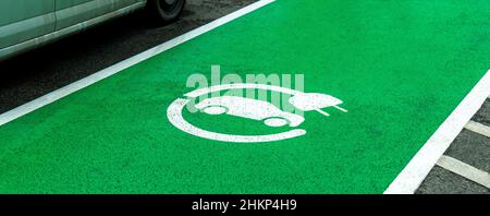 Leerer Parkplatz für Elektrofahrzeuge, grüne Zone markiert, Autoladegerätesymbol auf dem Asphalt, niemand. Umweltfreundlich, umweltfreundlich Stockfoto