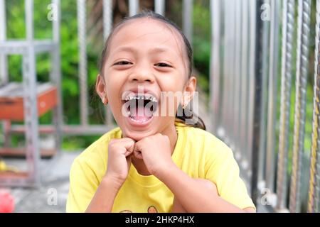 Lampung, Indonesien, Februar 05 2022- Ausdruck eines kleinen Mädchens mit weit geöffnetem Mund und gebrochenen Zähnen auf der Terrasse des Hauses. Selektiver Fokus. Stockfoto