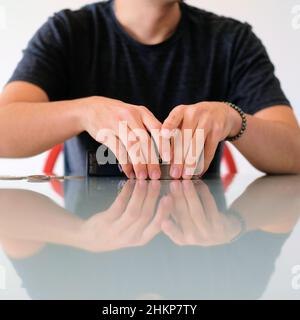 Junger Mann, der zu Hause Karten auf einem spiegelnden Küchentisch mit Glasplatte mischt und ausgibt; Familienabend mit Spielen. Stockfoto