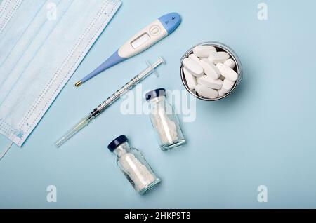 Thermometer zur Messung der Körpertemperatur, eine medizinische Maske, ein kleiner Eimer Pillen, eine Spritze zur Impfung. Stockfoto