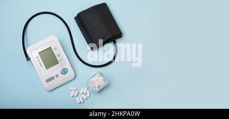 Ein Gerät zur Druckmessung, Tonometer auf blauem medizinischem Hintergrund und eine Reihe weißer Pillen. Kopfschmerzen, Behandlung von Bluthochdruck und Hypotensi Stockfoto