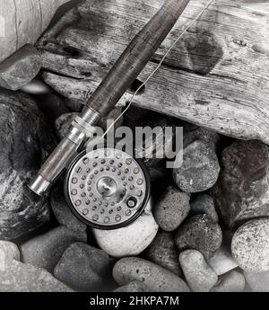 Antikes Fliegenrute und Rollen neben Stein und Treibholz mit Vintage-Effekt. Stockfoto