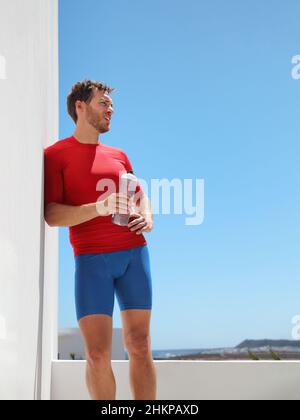 Sportler Mann Läufer trinken Sport Wasserflasche Training zu Hause Balkon oder im Freien Fitnessraum erschöpft mit Hitzschlag. Vertikale Ernte des muskulären Körpers Stockfoto