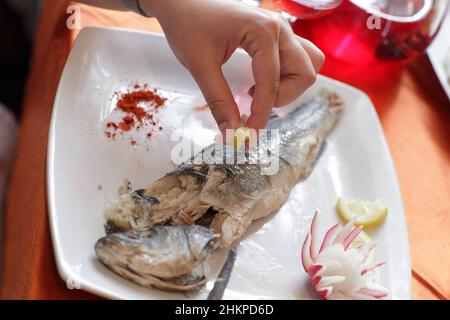 Die Frau quetscht den Saft aus einer Zitrone auf Fisch im Restaurant Stockfoto