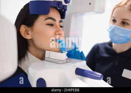 Weibliche Patientin machen einen zahnärztlichen Computertomographen. Der Radiologe führt einen CT-Scan des Kiefers durch. Frau, die in der Klinik eine Panoramaaufnahme der Zähne gemacht hat Stockfoto