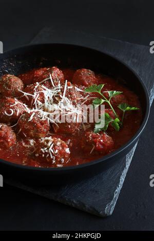Fleischbällchen mit Tomatensauce und Parmesankäse in einer Pfanne auf dunklem Grund. Direkt darüber. Stockfoto