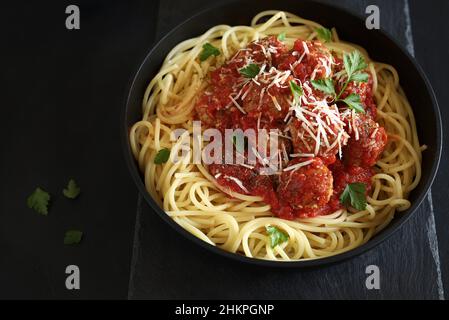 Spaghetti mit Fleischbällchen in Tomatensauce auf dunklem Hintergrund. Direkt darüber. Stockfoto
