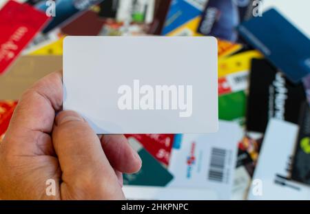 Leere Plastikkarte in der Hand auf verschwommenem Hintergrund verschiedener Plastikkarten Stockfoto