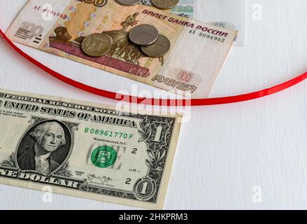 Rotes Band, das Banknoten einer US-Dollar-Banknote und russische Rubel mit Münzen auf weißem Hintergrund trennt Stockfoto