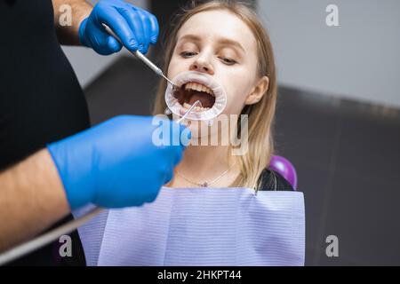 Der Zahnarzt spült die Mundhöhle des Patienten auf dem Zahnarztstuhl. Der Arzt behandelt die Zähne eines Patienten in einer Klinik für Stammatologie Stockfoto