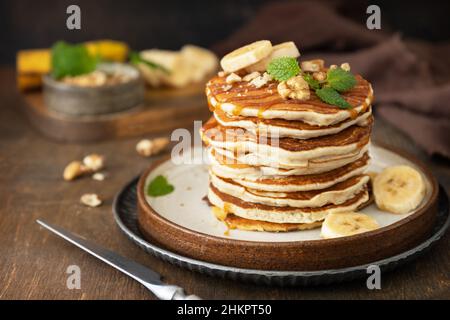 Wir feiern den Pfannkuchen-Tag, amerikanisches Frühstück. Köstliche hausgemachte Bananenpfannkuchen mit Nüssen und Karamell auf rustikalem Holztisch. Stockfoto