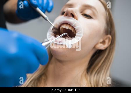 Der Zahnarzt spült die Mundhöhle des Patienten auf dem Zahnarztstuhl. Der Arzt behandelt die Zähne eines Patienten in einer Klinik für Stammatologie Stockfoto