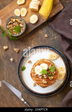 Wir feiern den Pfannkuchen-Tag, amerikanisches Frühstück. Köstliche hausgemachte Bananenpfannkuchen mit Nüssen und Karamell auf rustikalem Holztisch. Draufsicht flach liegend. Stockfoto