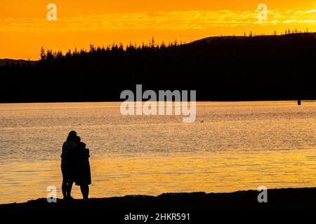 Romantik - eine Paarumarmung am Strand von Loch Morlich in der Nähe von Aviemore in den schottischen Highlands Stockfoto