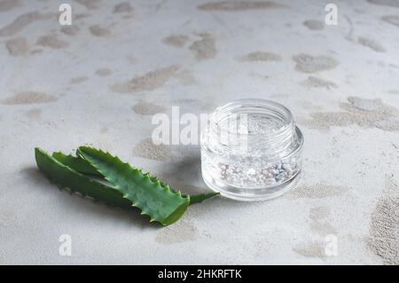 Transparentes Glas mit feuchtigkeitsspendender Creme mit Hyaluronsäure auf betonem Hintergrund Stockfoto