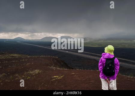 Ein einmunter Wanderer beobachtet den herannahenden Sturm, die Big Island, Hawaii, USA. Dunkle, bedrohliche Wolken sammeln sich am fernen Horizont. Saddle Road. Route 200. Stockfoto