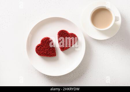 Valentinstag-Frühstück mit herzförmigem zwei roten Samtkuchen und Latte-Kaffee auf weißem Tisch. Blick von oben. Stockfoto