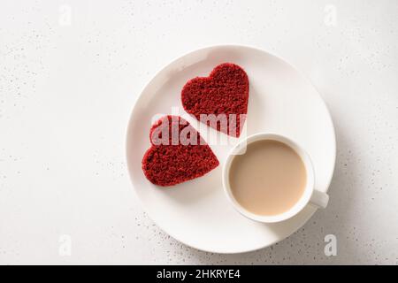 Valentinstag-Frühstück mit herzförmigem zwei roten Samtkuchen und Latte-Kaffee auf weißem Tisch. Blick von oben. Stockfoto