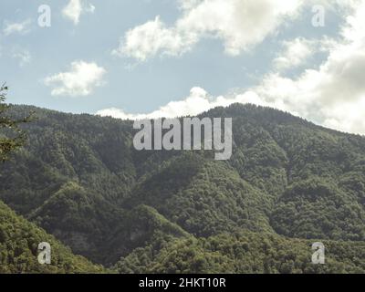 Grün bewaldete Bergkette vor einem blauen Himmel mit Wolken Stockfoto