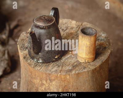 Ein alter verkohlter Wasserkocher mit selbstgemachtem Becher aus Holz steht auf einem Holzbalken. Teetrinken unter Feldbedingungen Stockfoto