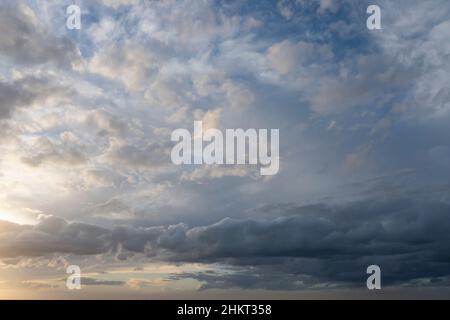 Luftwolkenlandschaft mit teilweise bewölktem Himmel über dem Himmel, Sonne bricht links durch die Wolken und dunkle Ominus-Sturmfront nähert sich unten rechts Stockfoto