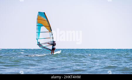 Ein Mann kontrolliert ein Segelboot auf See: Eines der besten Mittel gegen eine Pandemie ist Windsurfen, und es wird keine Maske benötigt! Stockfoto