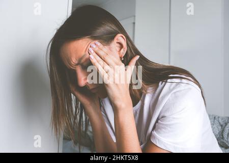 Junge Frau, die ihre Schläfe berührt und nach dem Aufwachen an Kopfschmerzen, Kopfschmerzen oder Migräne leidet Stockfoto