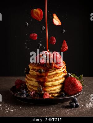 Stapel amerikanischer Pfannkuchen mit schwebenden Beeren und fallendem Karamell (cäceta). Kreative Levitation-Fotografie. Stockfoto