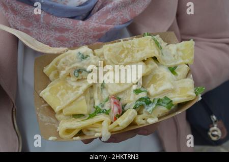 Die junge Frau isst Tagliatelle mit Käsesoße in einer Pappschale Stockfoto