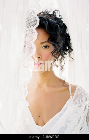 Porträt einer Frau in einem weißen Kleid, die hinter einem Vorhang aus guckt Stockfoto