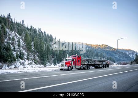 Professionelle Fracht roten klassischen großen Rig Semi-Truck Transport von Fracht auf dem langen Flachbett Sattelanhänger bergauf auf auf die Wicklung gefährlichen Slip Stockfoto