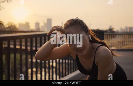 Junge Sportlerin, die nach einem Cardio-Training bei Sonnenuntergang in der Stadt erschöpft in Ruhe läuft. Jogging Lebensstil gesund. Stockfoto