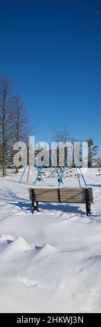 Panorama-Vertikalfoto der Schaukel - Kinder Spielbereich Ausrüstung mit Schnee bedeckt mit Parkbank im öffentlichen Park. Vertikales Format Hintergrund pho Stockfoto