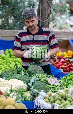 Ein türkischer Gemüsehändler schneidet Brokkoli auf dem Kas Freitagsmarkt. KAS ist ein Dorf, das am Mittelmeer der Türkei liegt. Stockfoto