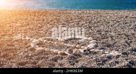 Liebe Herzform auf Sand aus weißen Kieselsteinen, Symbol der Liebe am Strand mit Meereshintergrund. Valentinstag Liebe Symbol der Herzform, Liebe Stockfoto