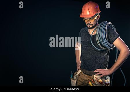 Elektriker mit Elektrokabel auf schwarzem Hintergrund, Kopierraum. Stockfoto